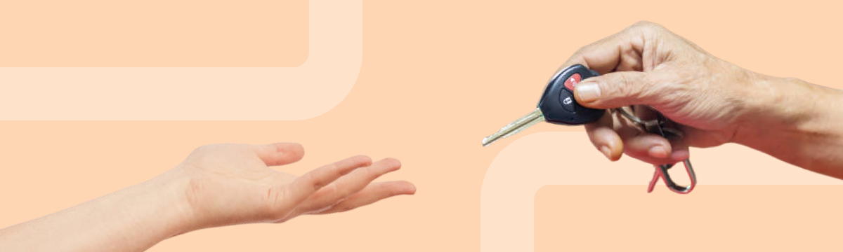 Close-up of one hand holding out a car key toward another person’s open hand against a peach-colored background.